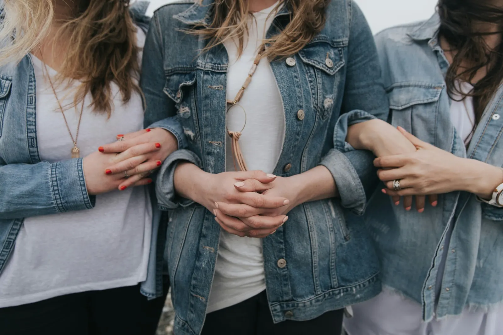 Three women in denim jackets standing close with their arms linked